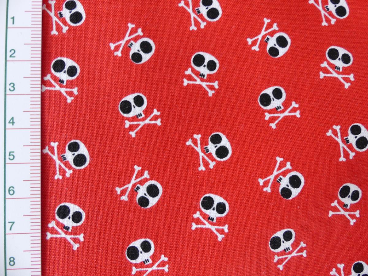 Stoff in rot mit vielen, kleinen, weißen Totenköpfen von Riley Blake. Detailansicht mit Maß
